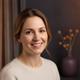 Headshot portrait of a happy woman in her 30s smiling confidently, with a soft, blurred background in deep charcoal and plum.